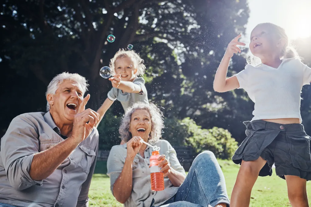 Grandparents and two young girls playing with bubbles in a park.