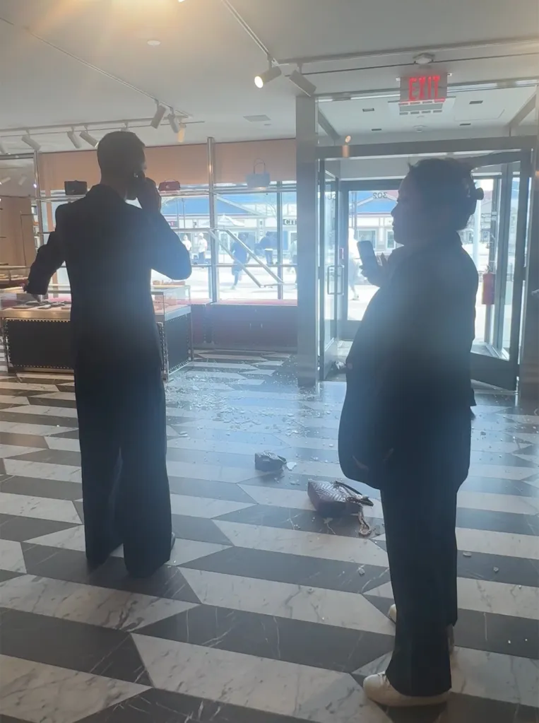 Two people stand inside a ransacked Gucci store with shattered glass on the floor.
