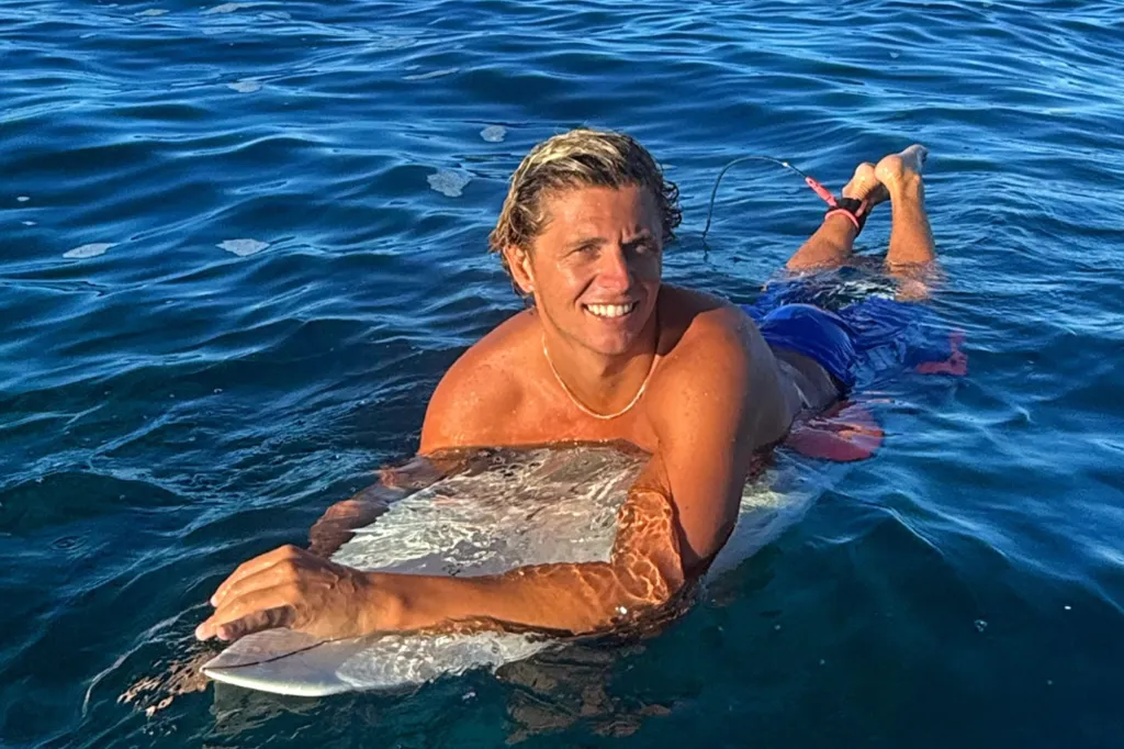 Guy Rowles, an Australian surfer, lying on his surfboard in the water and smiling.