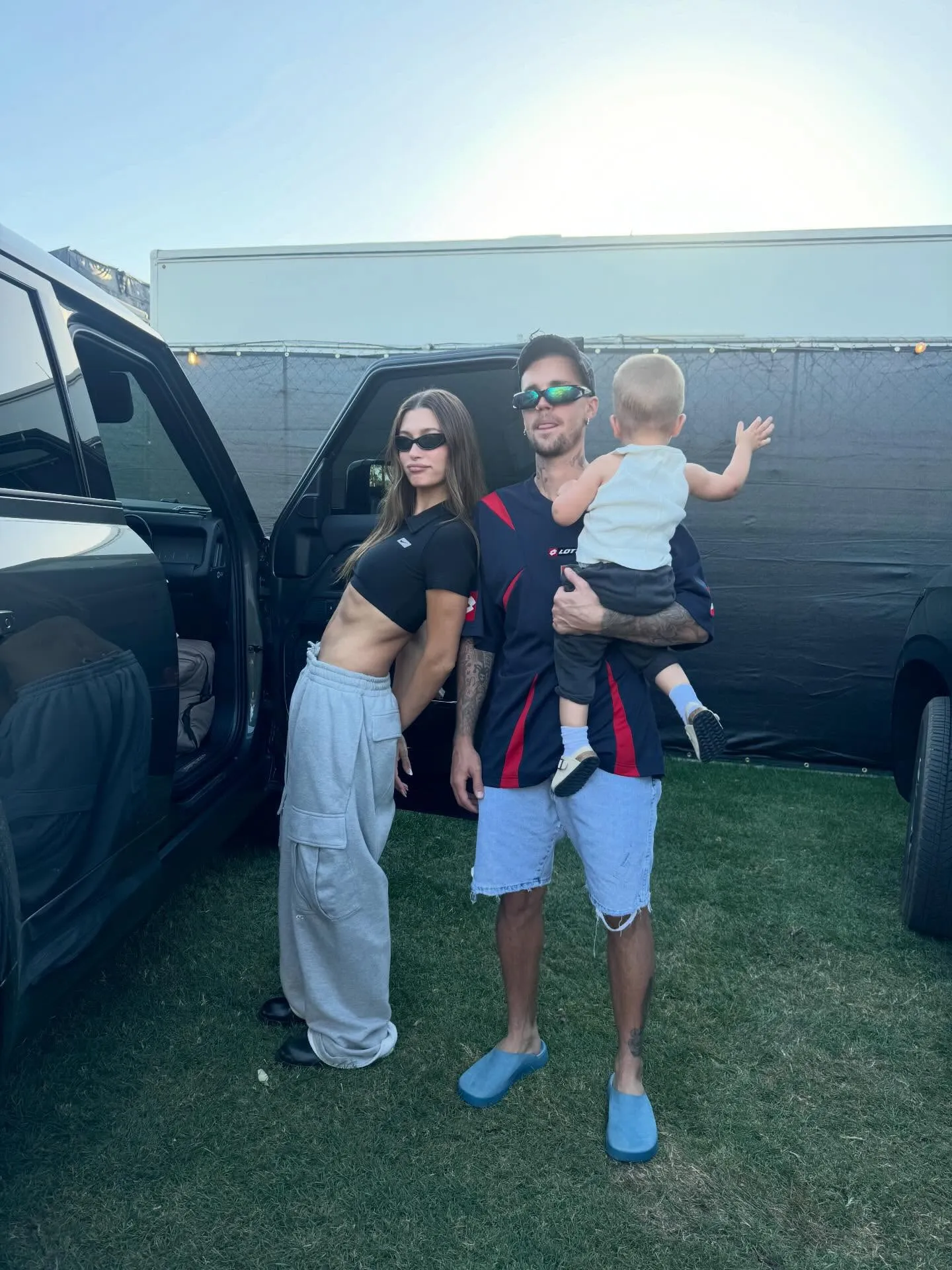 Hailey Bieber leans against a car while Justin Bieber holds Jack Bieber.