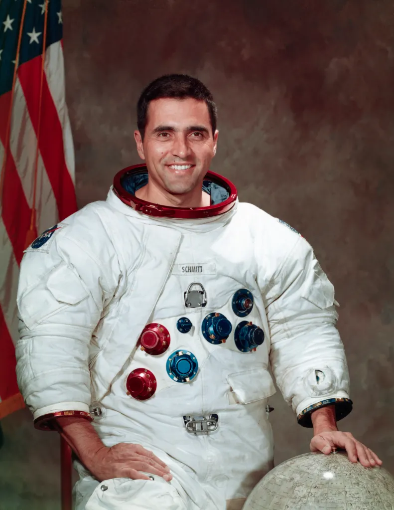 Harrison Schmitt, lunar module pilot for Apollo 17, in a spacesuit with an American flag behind him.