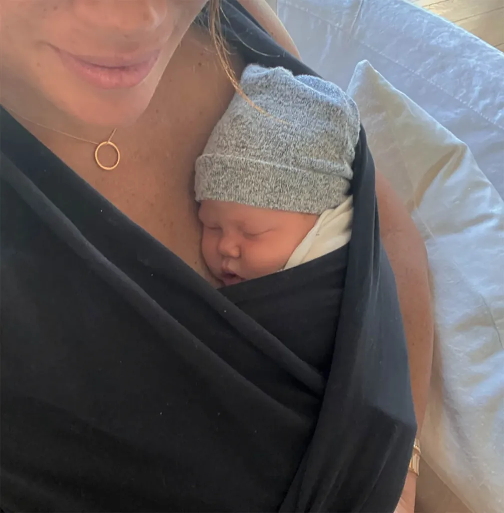 Meghan Markle holds newborn Lilibet in a dark baby carrier, with Lilibet wearing a gray knit hat.