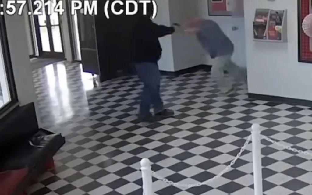 Surveillance footage shows a man in a black hoodie holding a gun, pointing it at another man in a blue shirt and light-colored pants.