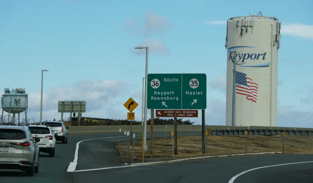 Highway exit signs direct drivers toward Keyport, Keansburg, and Hazlet near a visible water tower on a curved roadway.