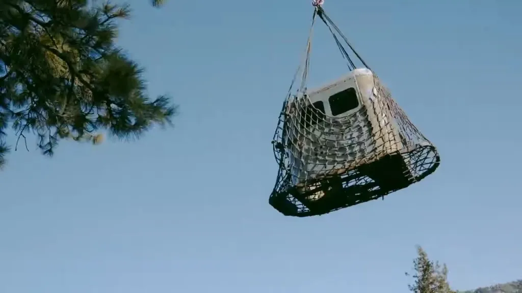 A historic gondola cabin is lifted by a net against a clear blue sky.