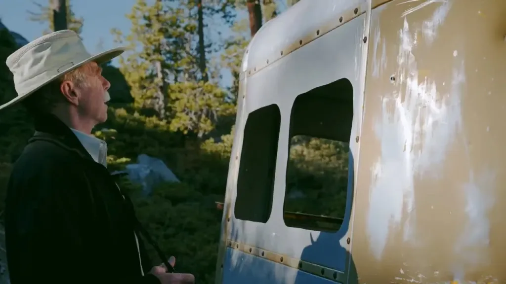 A man in a hat looking at a historic gondola cabin in the woods.