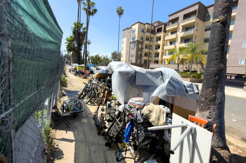 Homeless encampment on a sidewalk across from a building that reads 