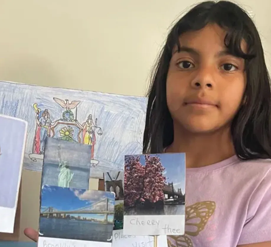 A young girl holds up a school project featuring images of New York landmarks.