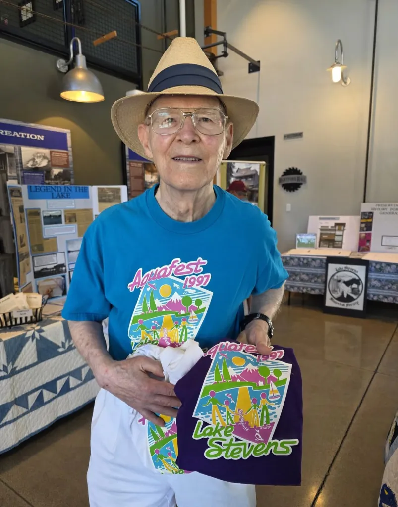 Roger Sweet, creator of He-Man and Masters of the Universe, holding two Aquafest 1997 Lake Stevens t-shirts.