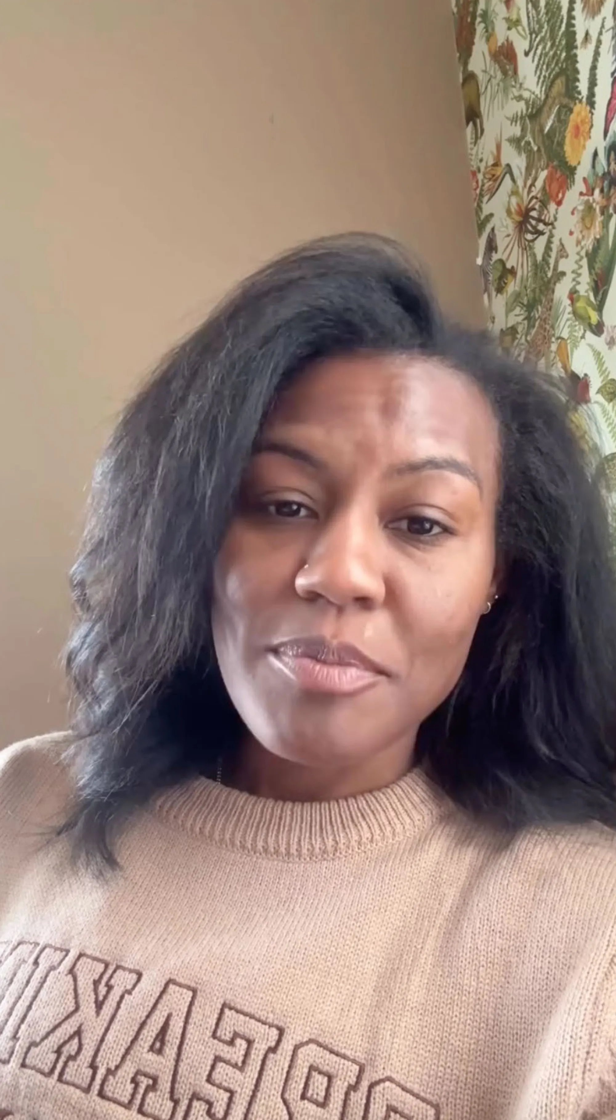 A close-up of a woman with dark hair wearing a light brown sweater.