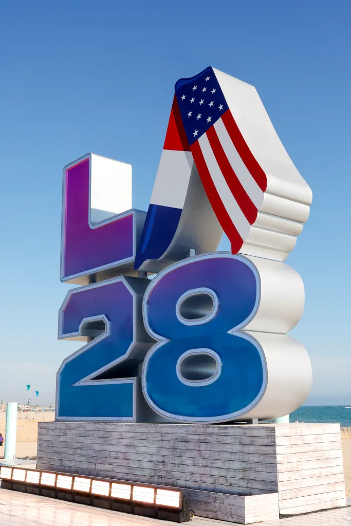 LA28 Olympic Games signage on a beach with an American flag draped over it.