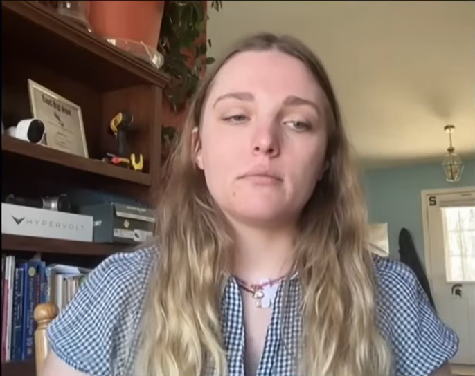 A young woman with long blonde hair and a plaid shirt looking at the camera.