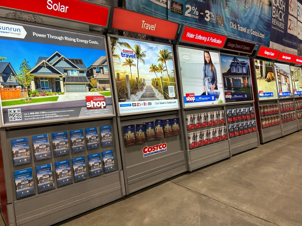 Information kiosks at Costco advertising solar panels, travel deals, water purification, garage doors, flooring, and home organization.