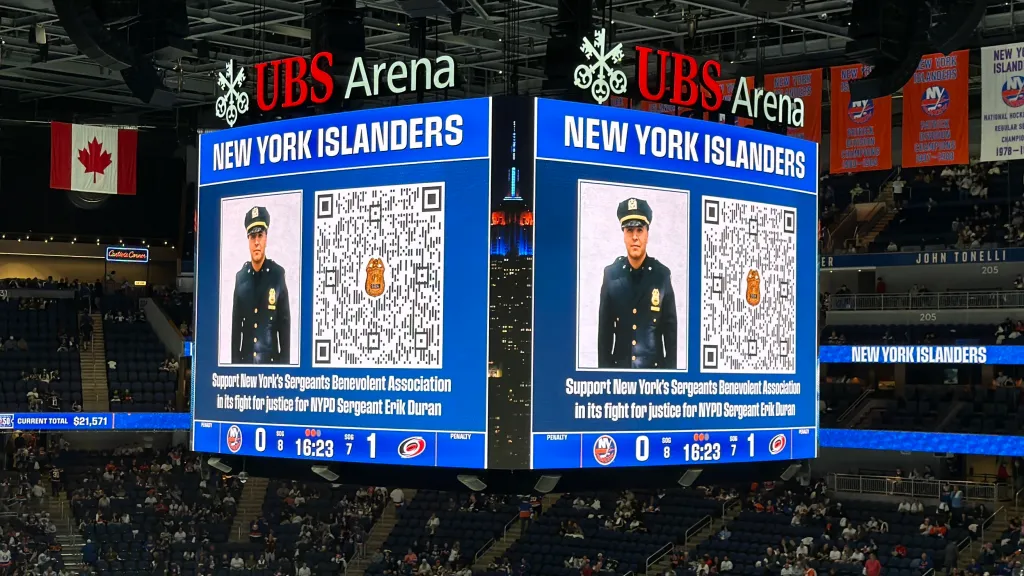 Jumbotron at UBS Arena displaying a photo of NYPD Sergeant Erik Duran, a QR code, and text supporting his legal fund during a New York Islanders game.