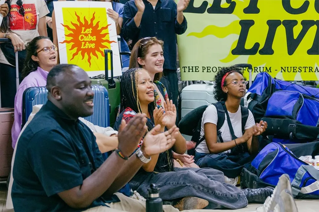 Isra Hirsi and others from the Let Cuba Live Youth Brigade arriving in Cuba, clapping and smiling, with luggage around them and a 