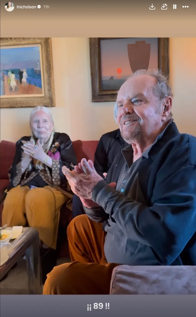 Jack Nicholson and another individual sitting on a couch, clapping.