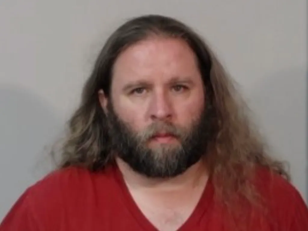 A mugshot of Branton. He has long hair.