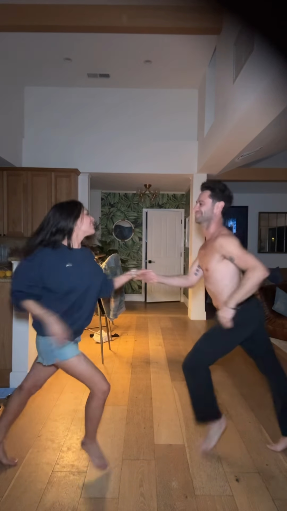 Janel Parrish and Sasha Farber performing a salsa dance in a living room.