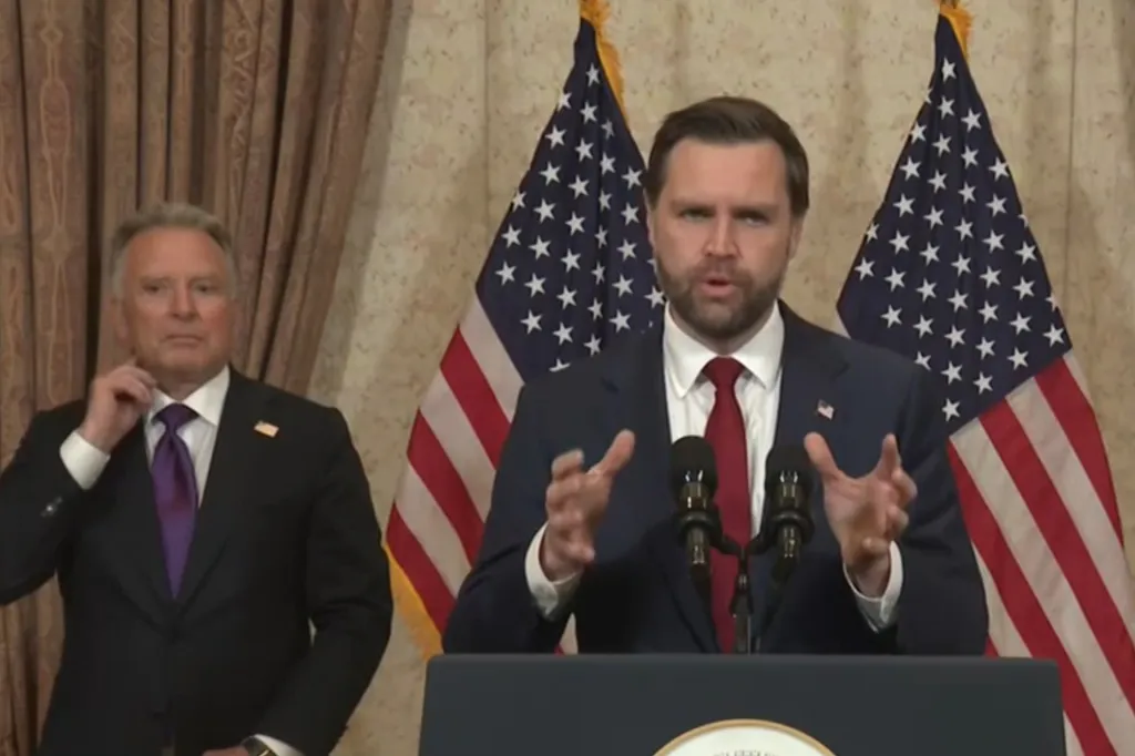 JD Vance speaking at a podium with two American flags behind him.