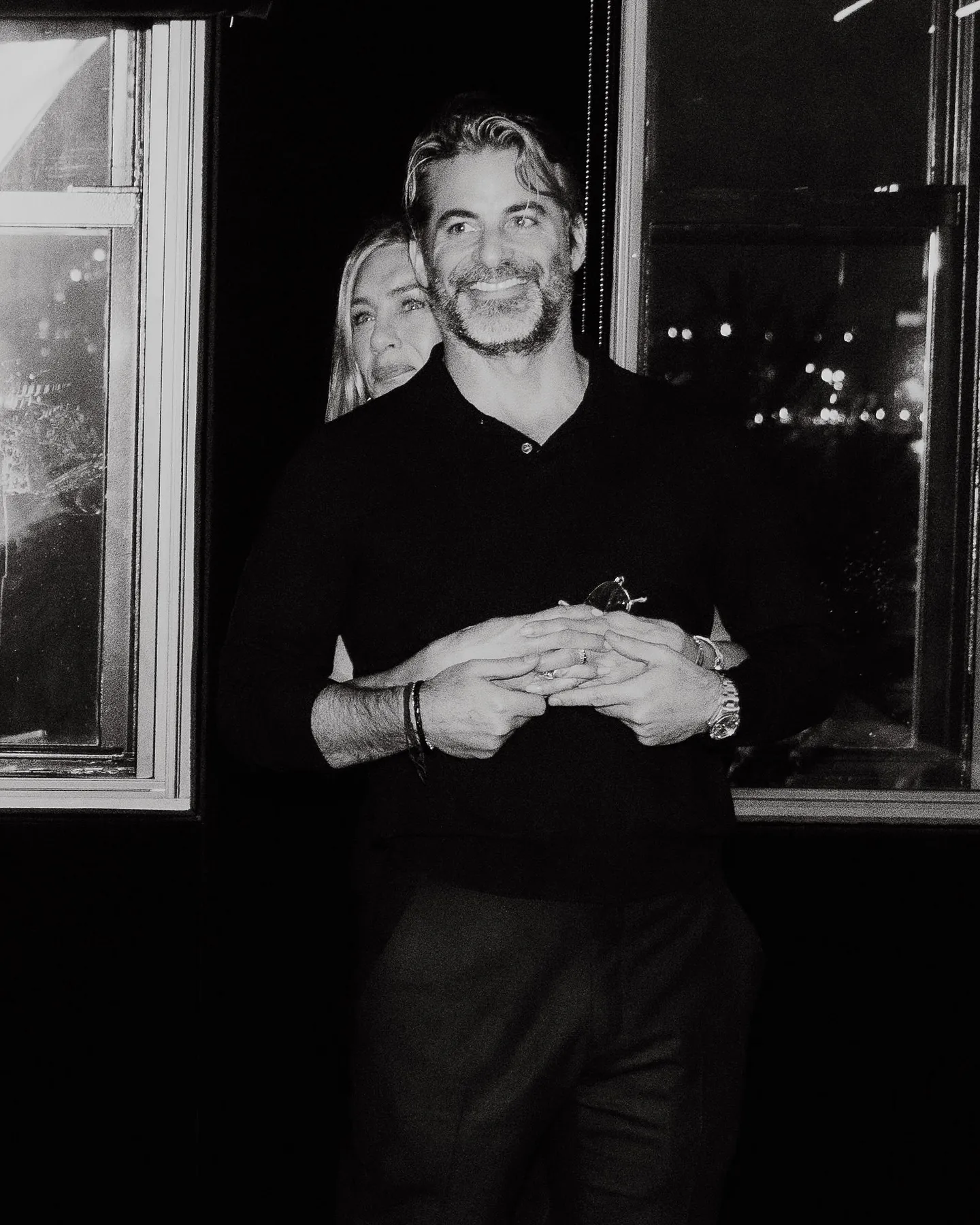 Jennifer Aniston embracing Jim Curtis from behind, holding his hands, with both smiling.