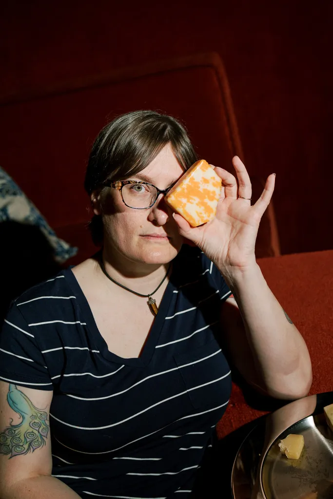 Jennifer Billock, known as the Cheese Witch or Jen the Tyromancer, holds a piece of marbled cheese up to her eye.