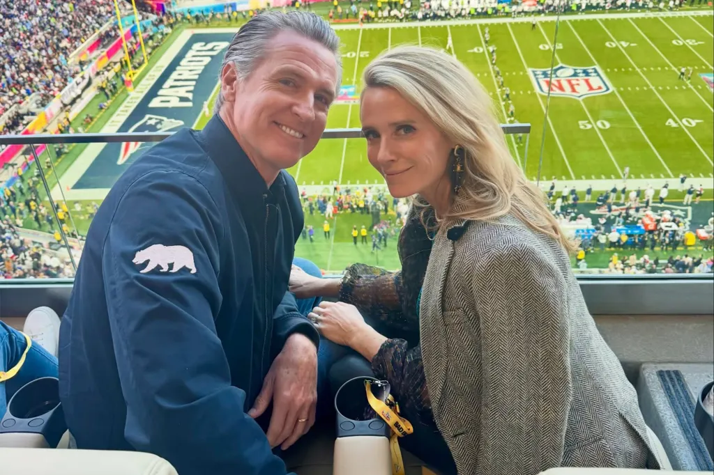 Gavin Newsom and Jennifer Siebel Newsom smiling at a football game.