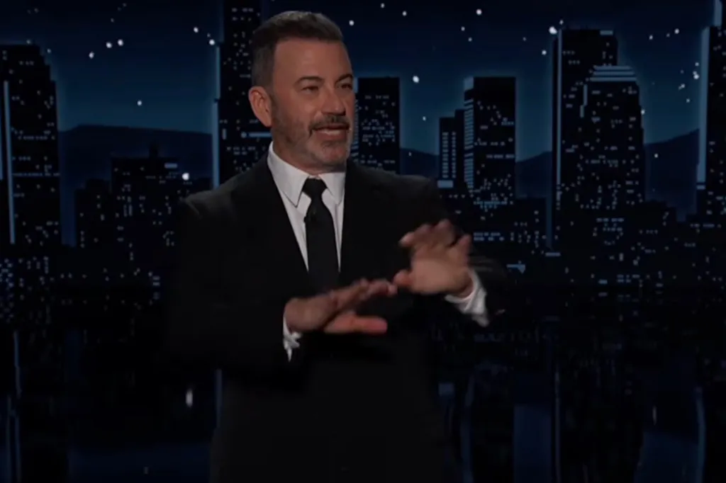 Jimmy Kimmel wearing a black suit and black tie, gesturing with his hands.