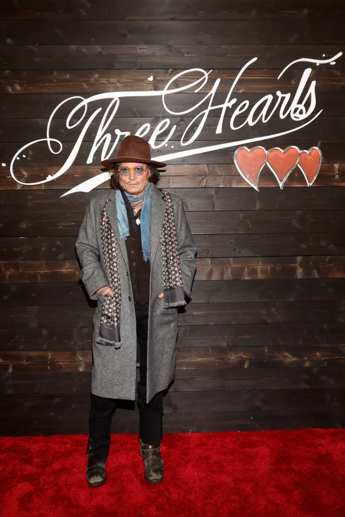 Johnny Depp standing on a red carpet in front of a dark wooden wall with 