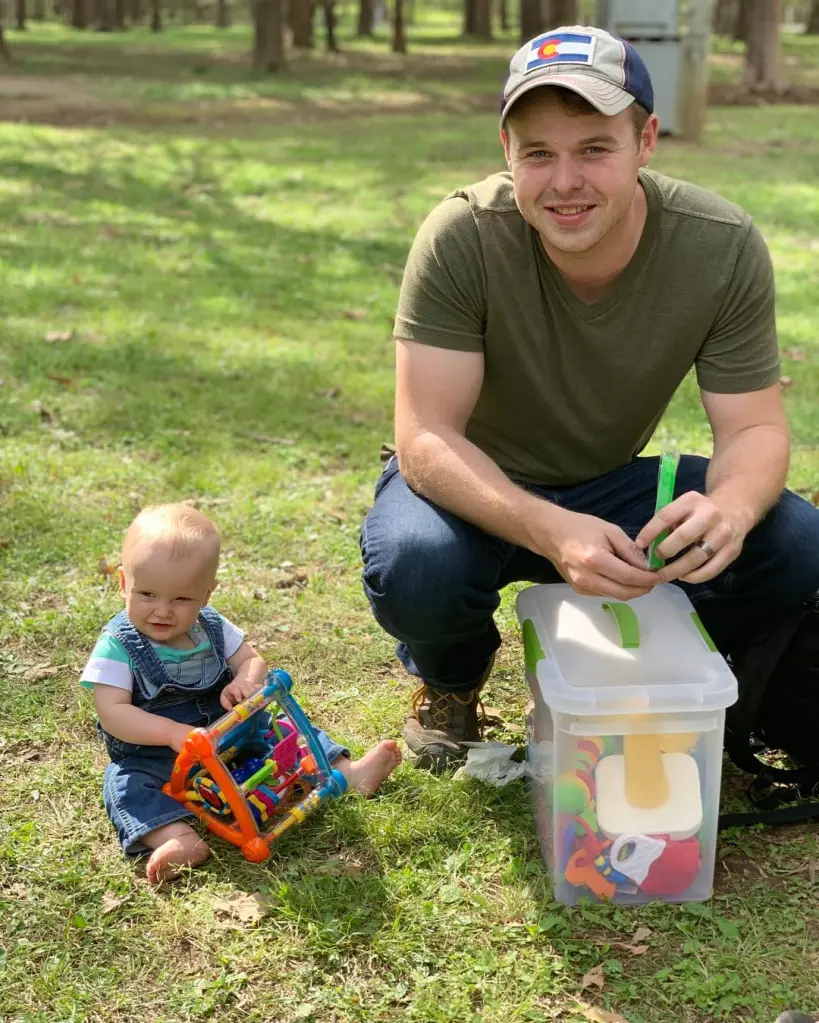 Joseph Duggar and his baby son, Garrett, sitting on the grass in an outdoor setting.