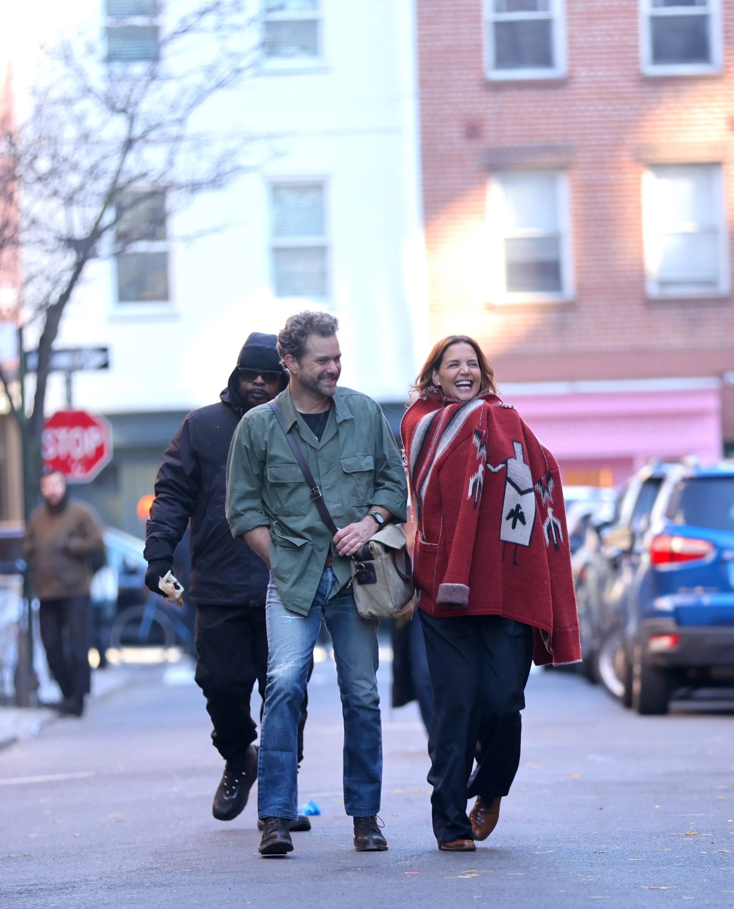 Joshua Jackson and Katie Holmes smiling while walking on a movie set.
