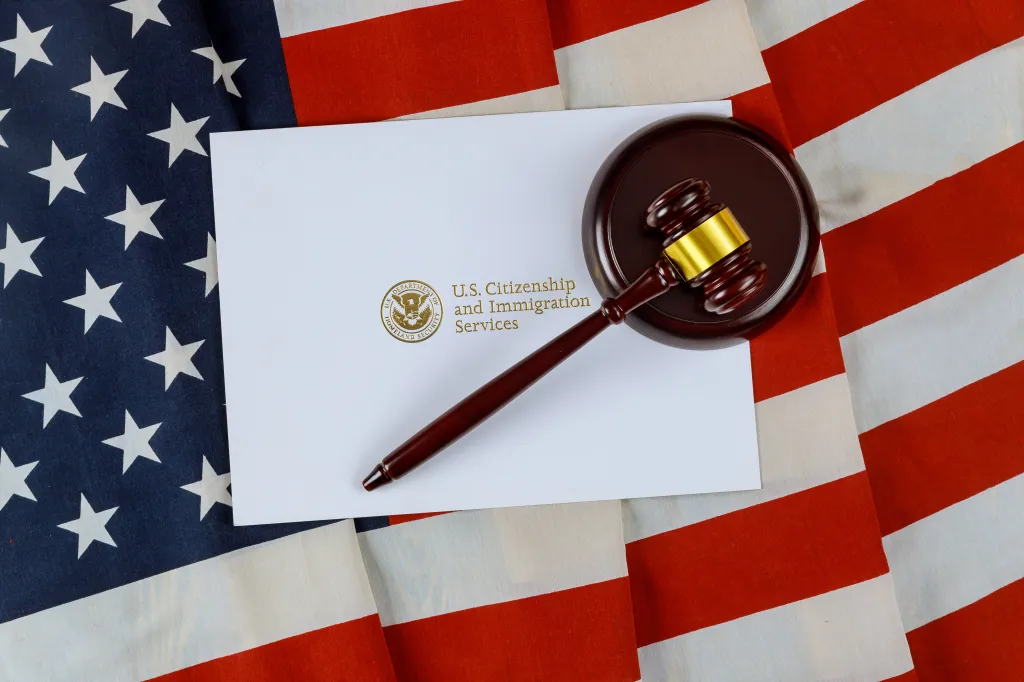 A gavel on top of an envelope from U.S. Citizenship and Immigration Services, all resting on an American flag.