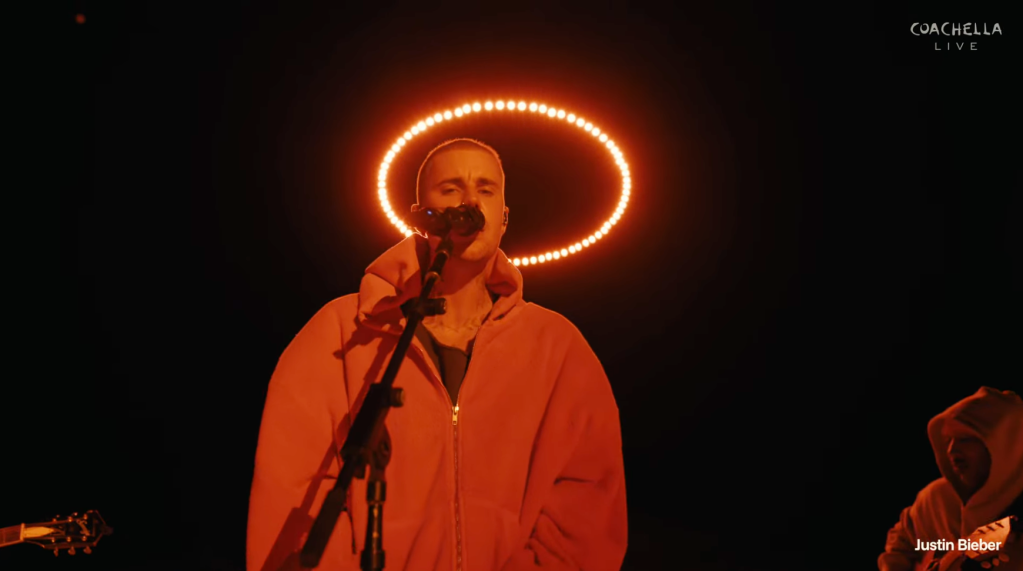Justin Bieber singing into a microphone on stage, with an orange halo of light behind his head.