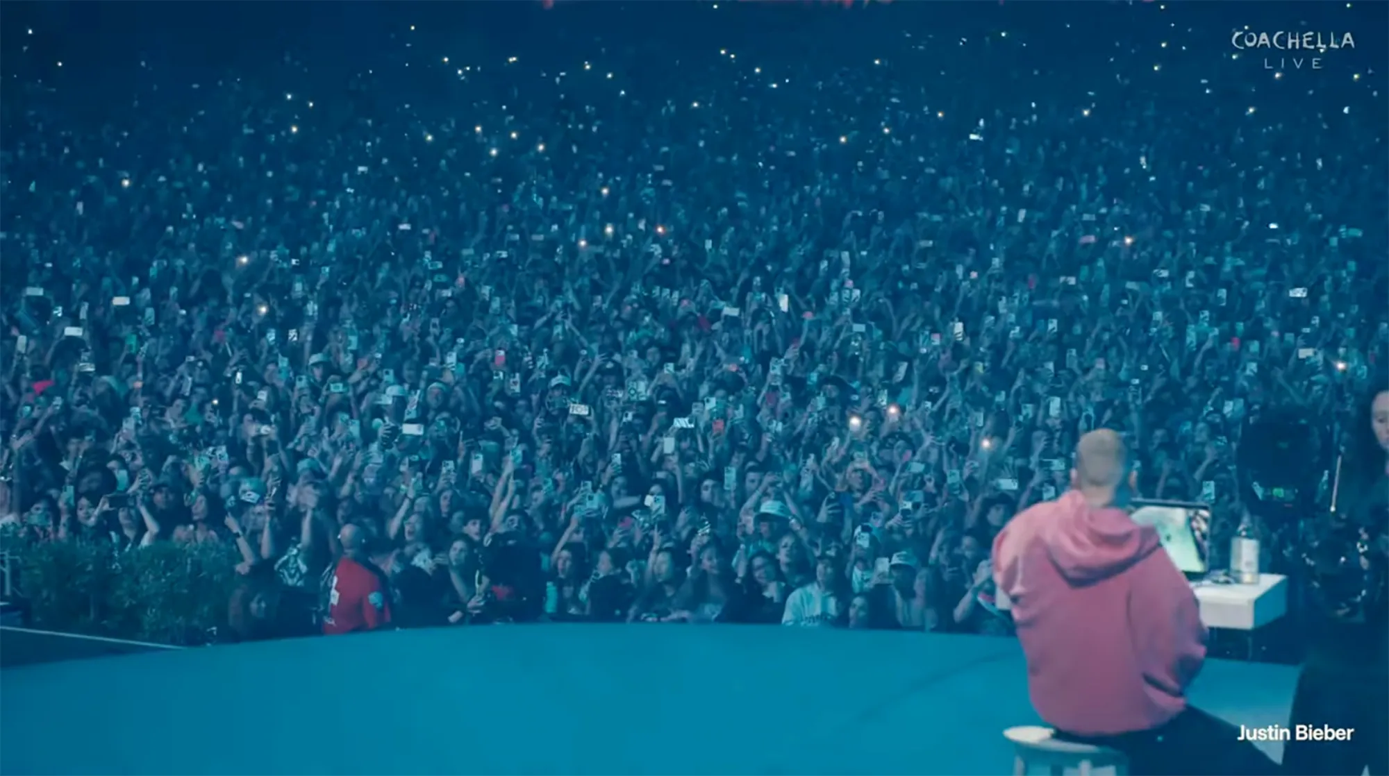 Justin Bieber performing on stage in front of a large crowd holding up phones.