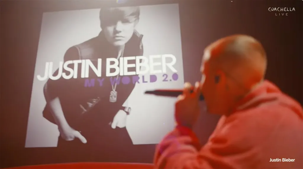Justin Bieber performing at Coachella, with a large screen behind him displaying the cover art for his album 