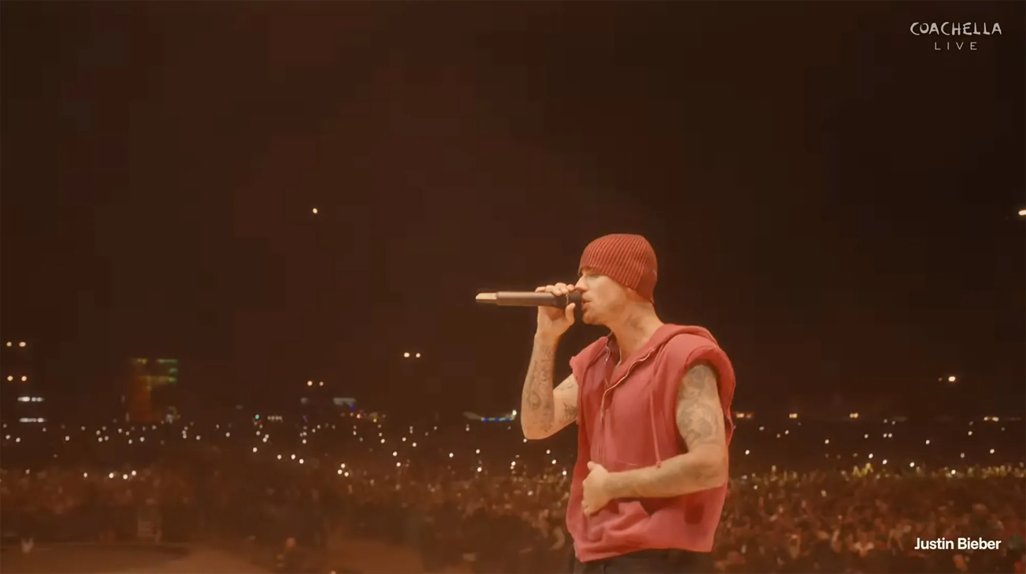 Justin Bieber singing into a microphone on stage at Coachella, with a crowd visible in the background.
