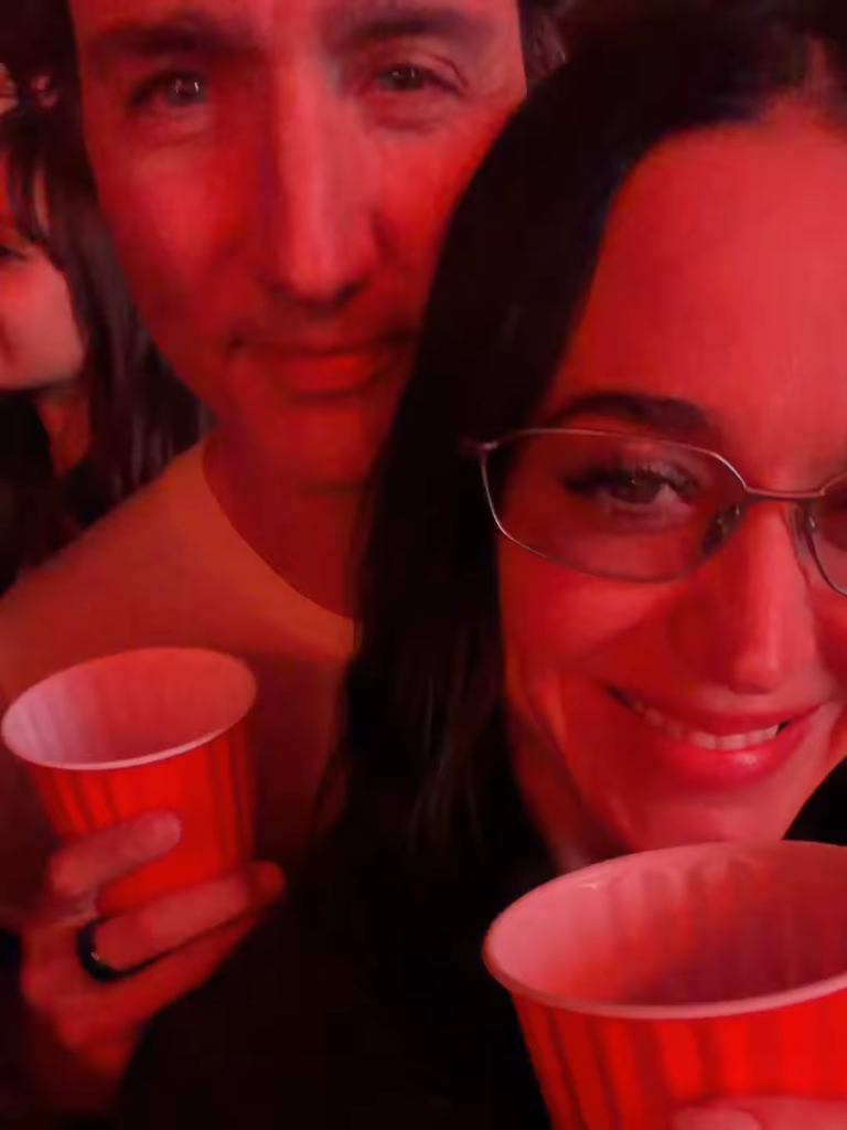 Justin Trudeau and Katie Perry holding red cups under red light at the Coachella Valley Music and Arts Festival.