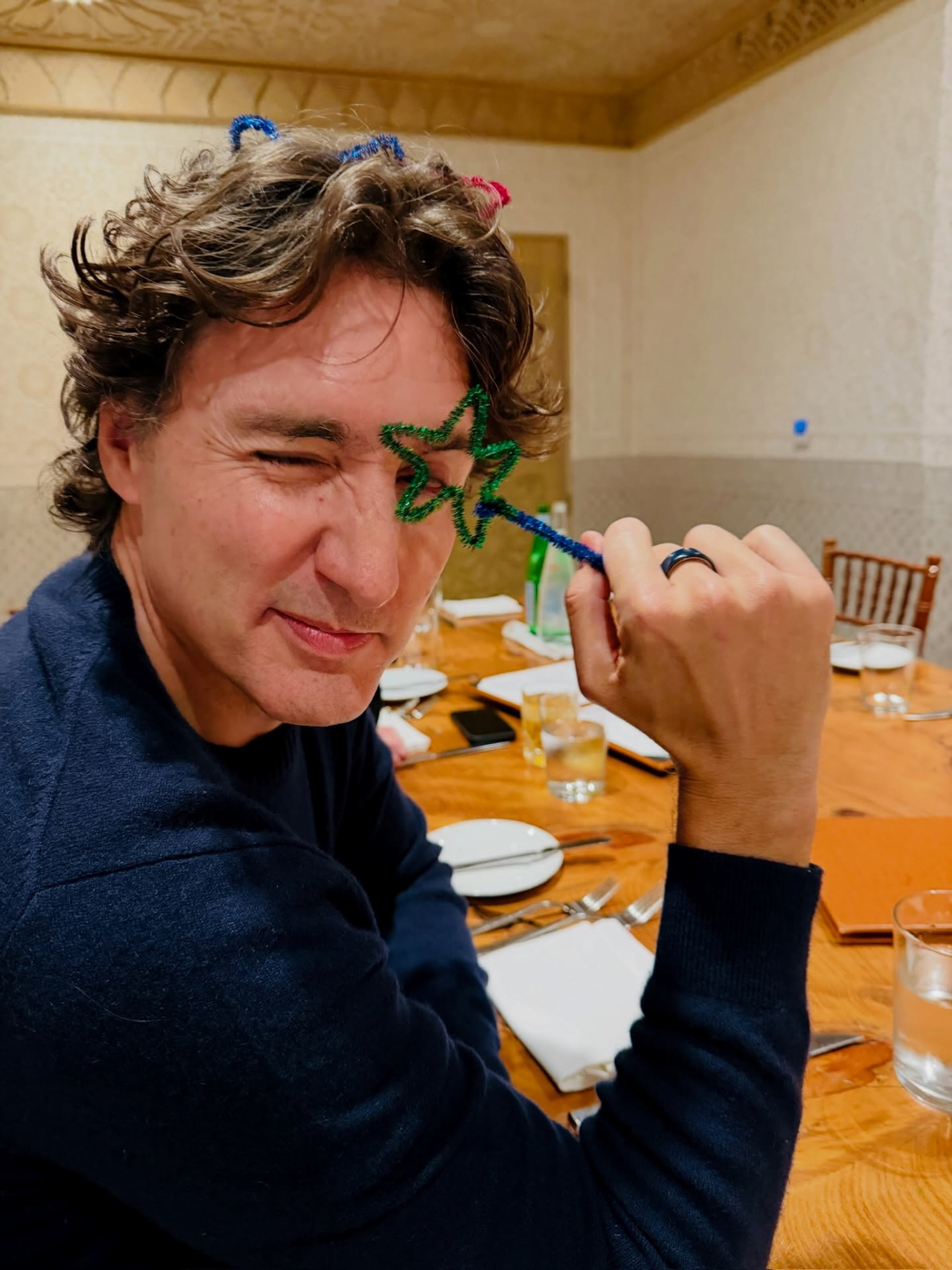 Justin Trudeau winking while holding a green pipe cleaner star over his eye.