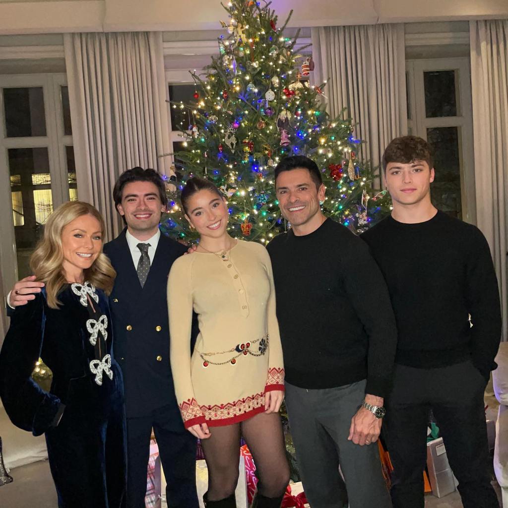 Kelly Ripa, Mark Consuelos, and their three children standing in front of a Christmas tree.
