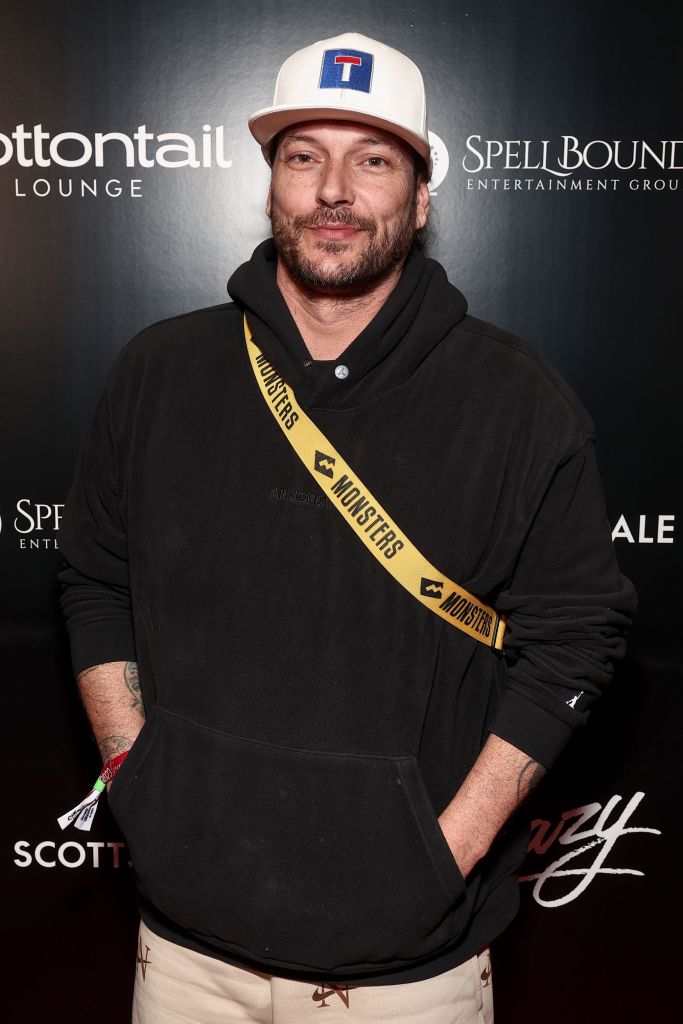 Kevin Federline wearing a white baseball cap, a black hoodie, and a yellow 