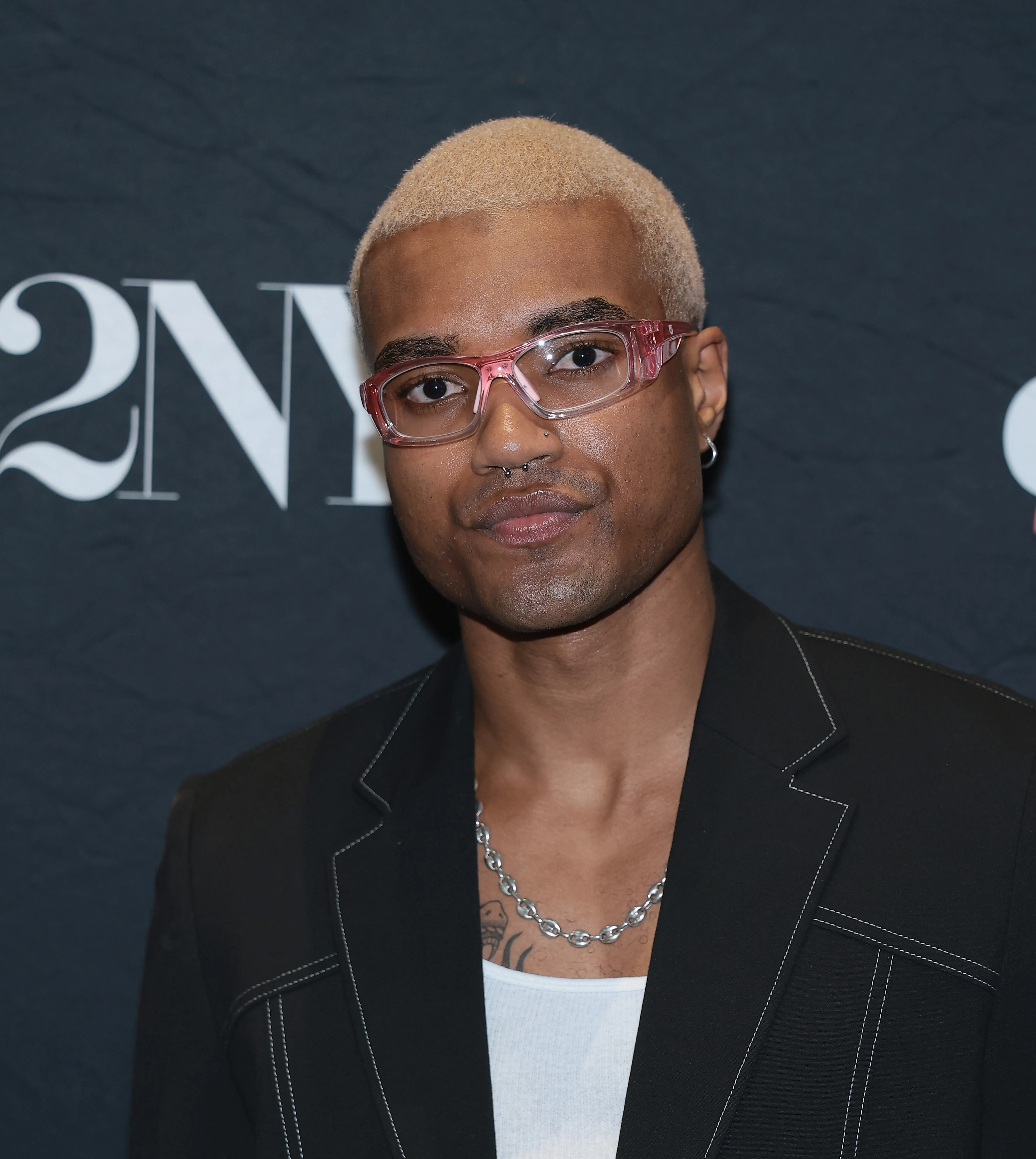 KJ Dillard wearing pink framed glasses and a black jacket over a white undershirt.