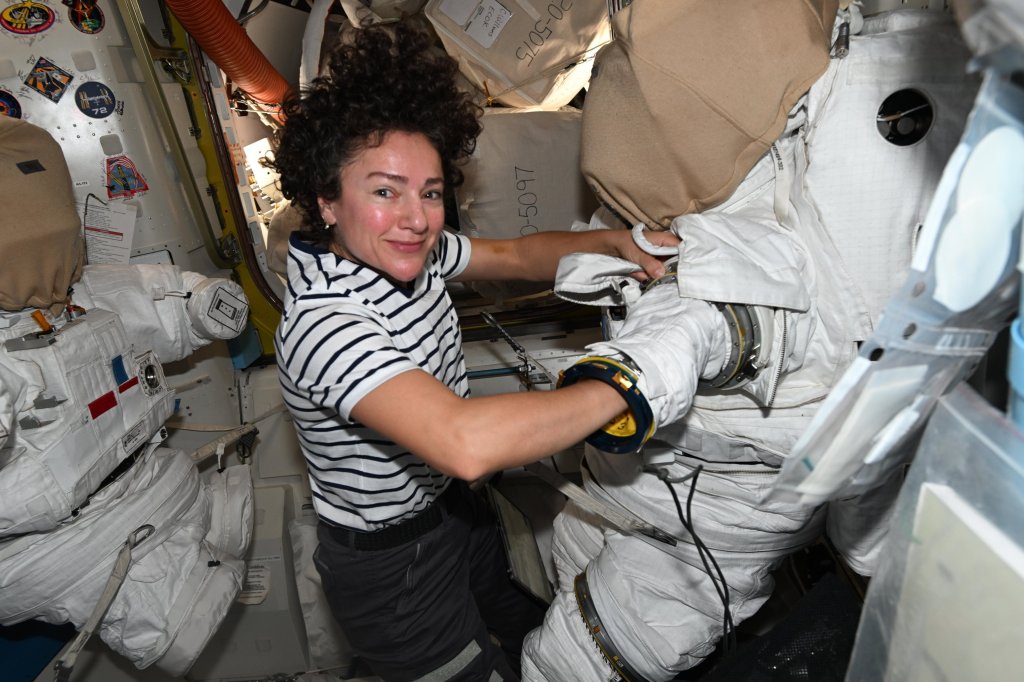 Astronaut Jessica Meir inside the International Space Station, smiling while working with a spacesuit.