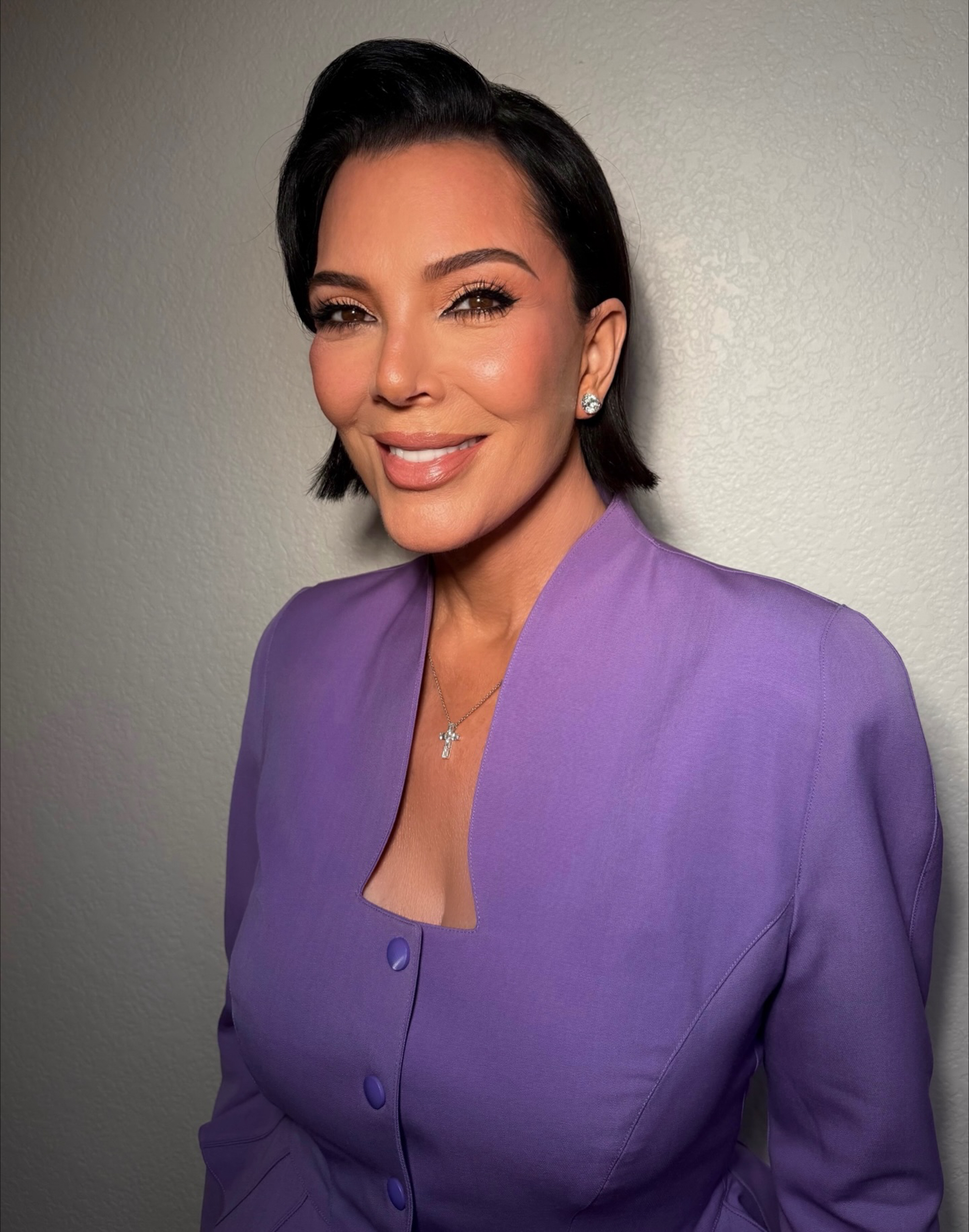 Kris Jenner in a purple button-down top with a square neckline, looking at the camera.