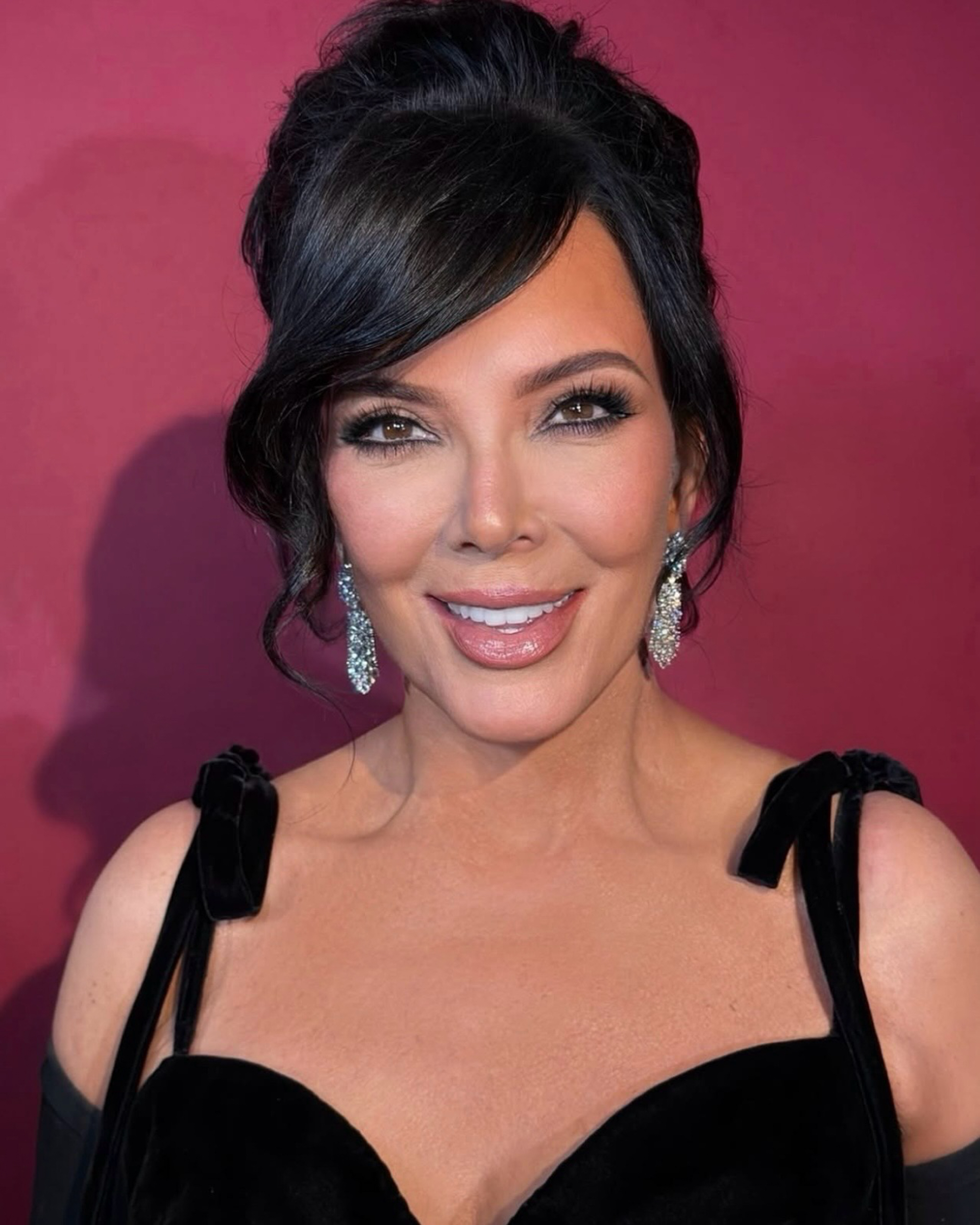 Kris Jenner smiling in a black velvet dress and sparkling earrings.