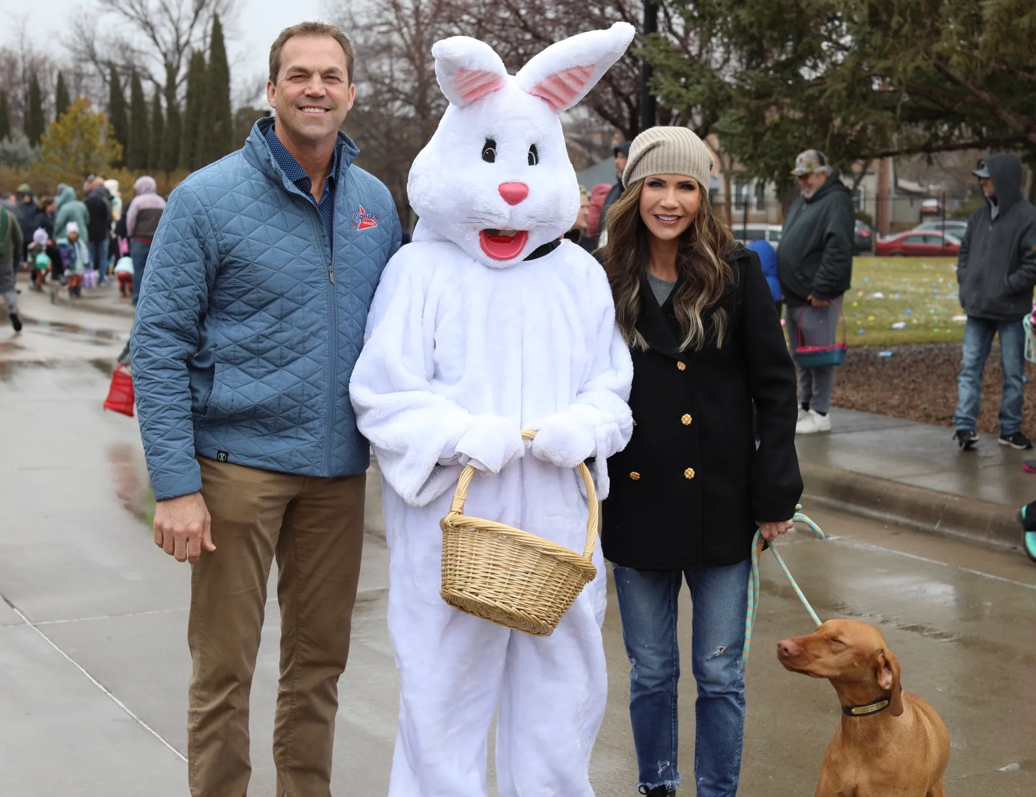 Kristi and Bryon pose with an Easter Bunny mascot, and a dog sits next to one of the adults.