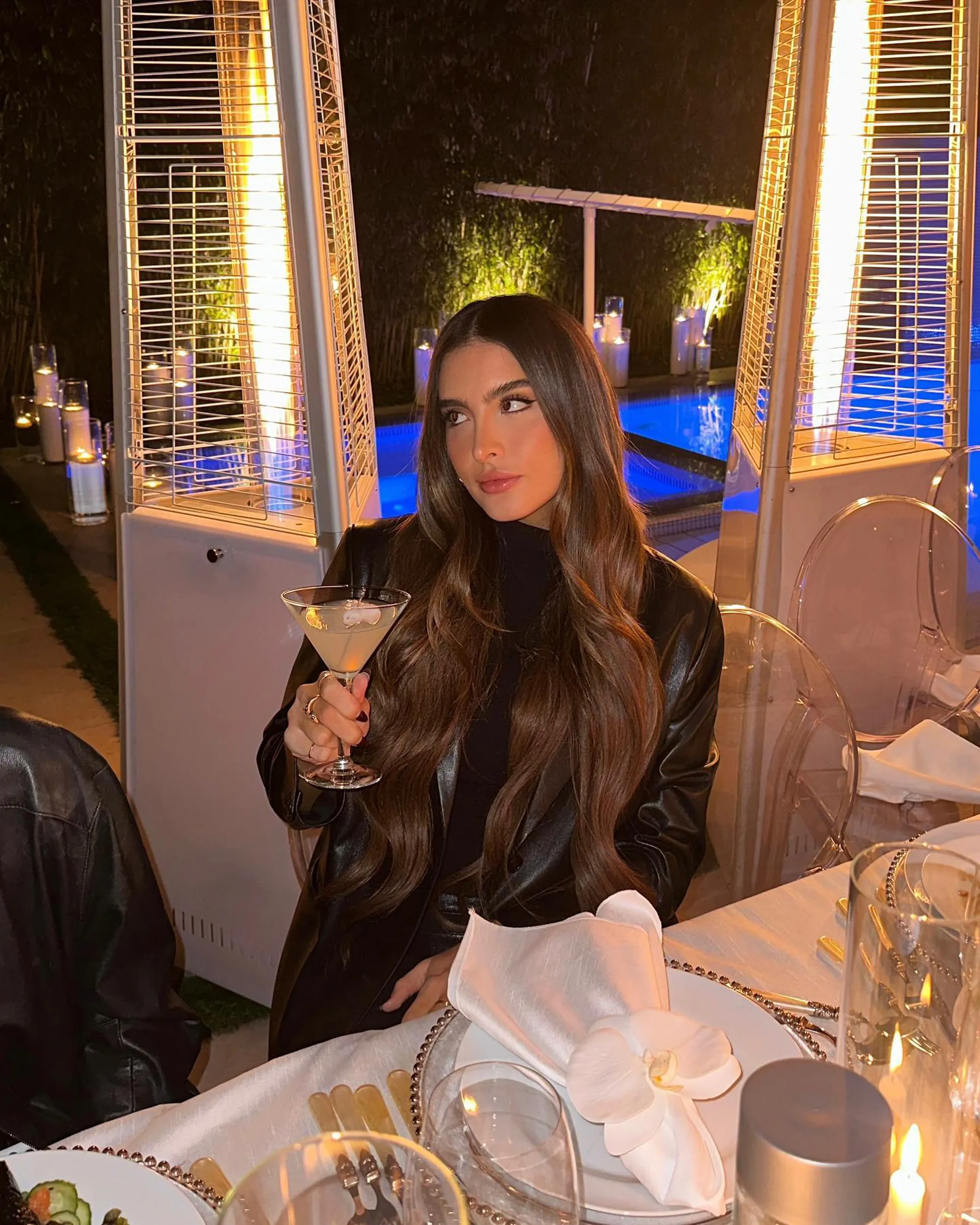Sophia Umansky holding a cocktail at an outdoor dining table at night.