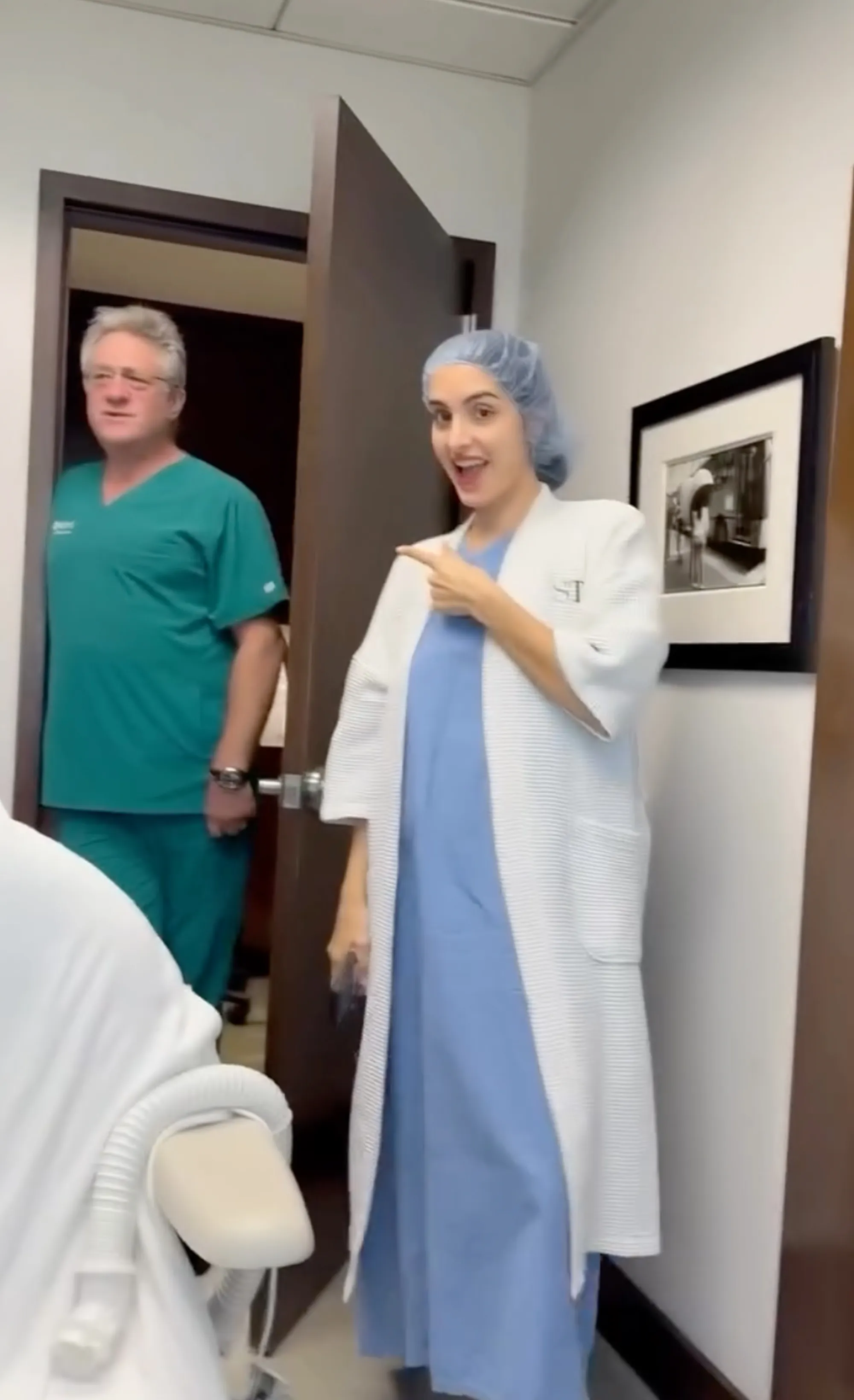 Sophia, Kyle Richards' daughter, in a hospital gown and hairnet, laughs in an exam room while a doctor in teal scrubs peeks through an open doorway.