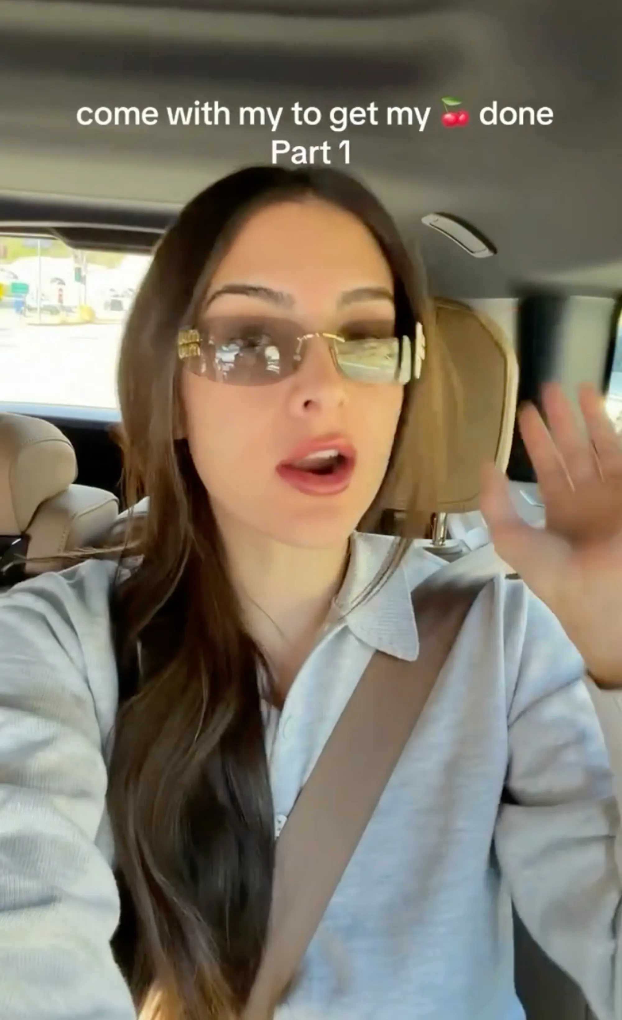 Sophia Umansky in a car, wearing a light gray long-sleeved shirt and sunglasses, caption reads 