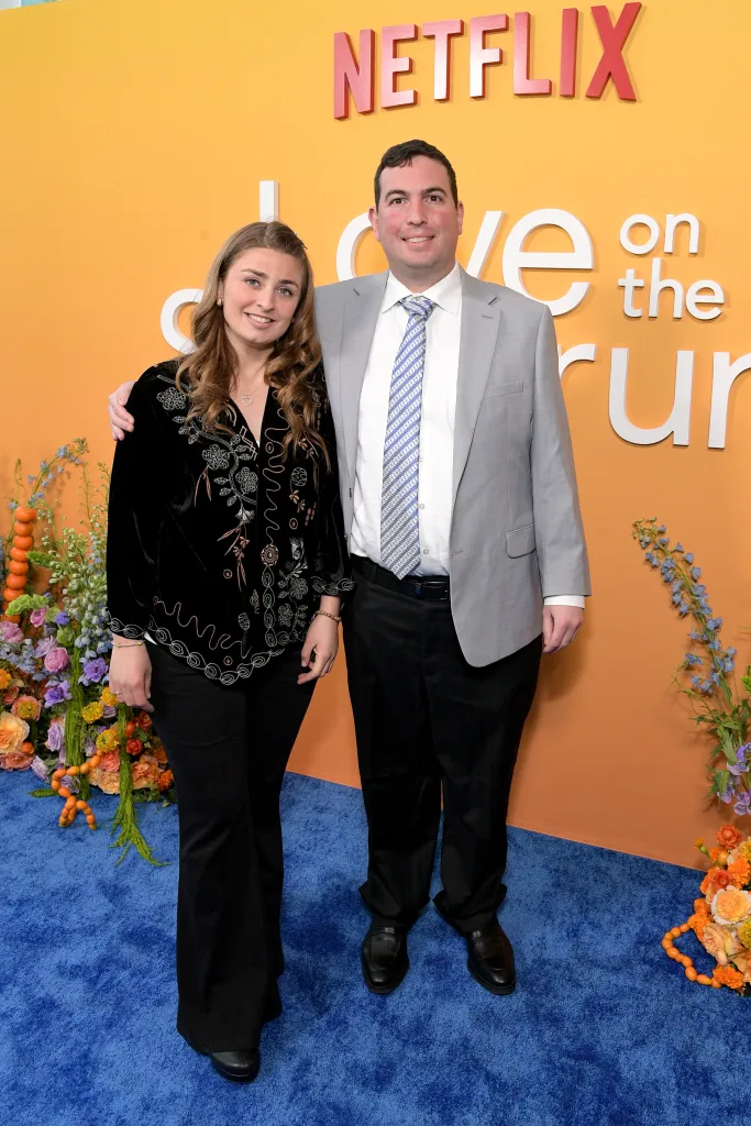 Abbey Lutes and David Isaacman pose on a blue carpet in front of an orange background with the Netflix logo and “Love on the Spectrum” in white lettering.