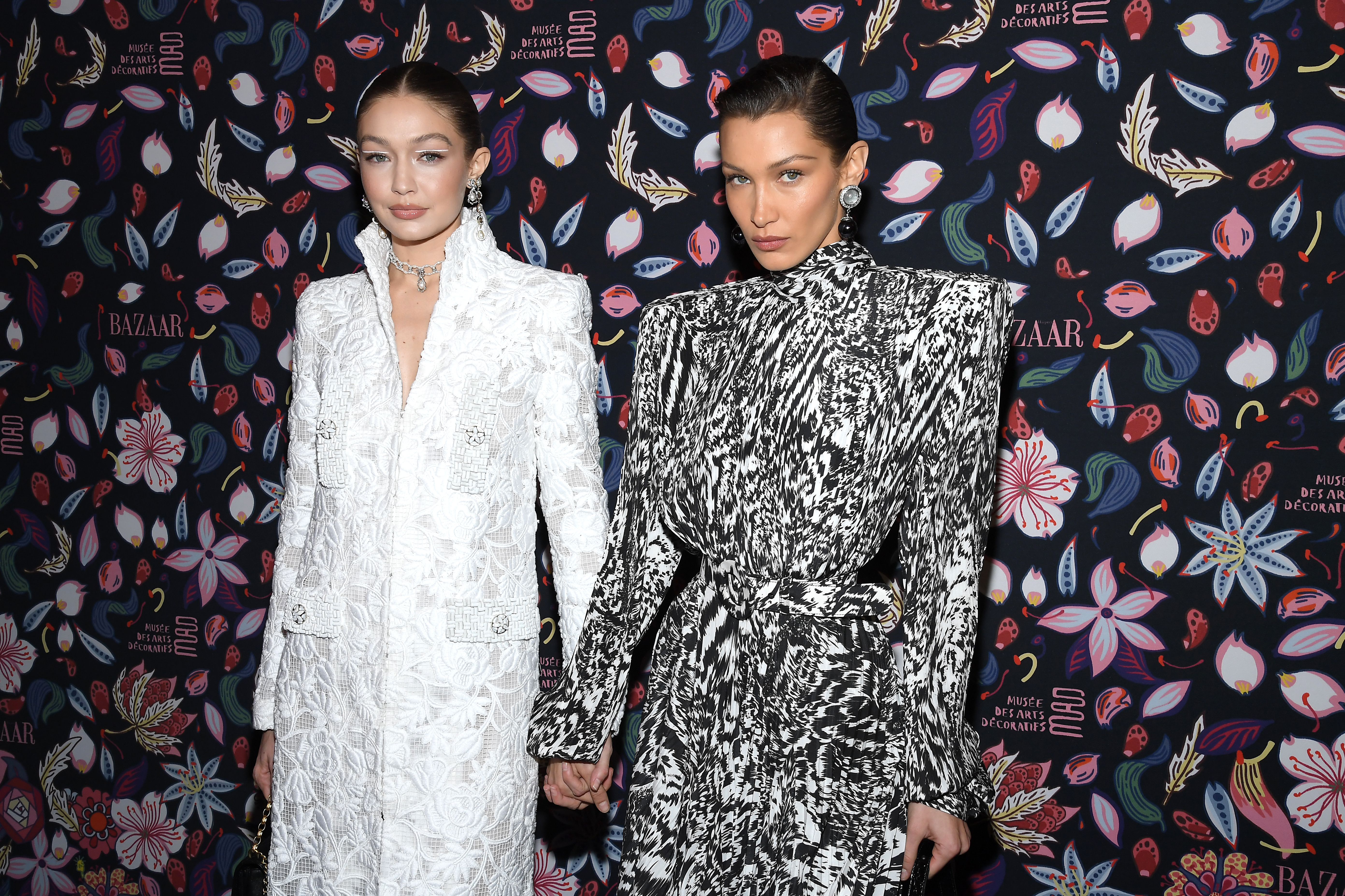 Gigi Hadid in white and Bella Hadid in black and white attend the Harper's Bazaar Exhibition.