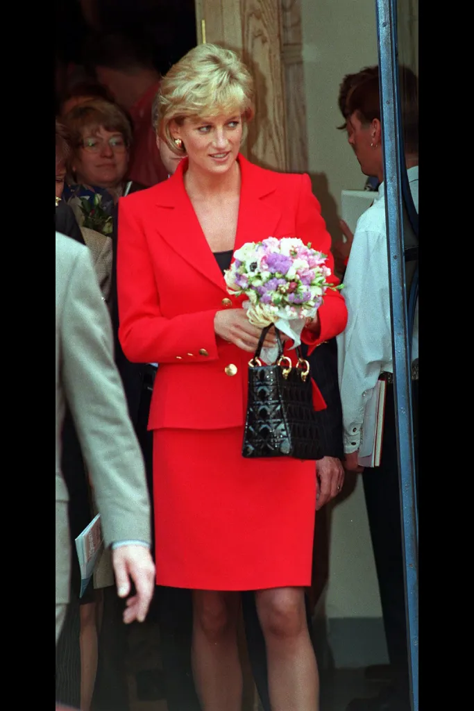 Princess Diana in a red skirt suit, holding a bouquet and black handbag.